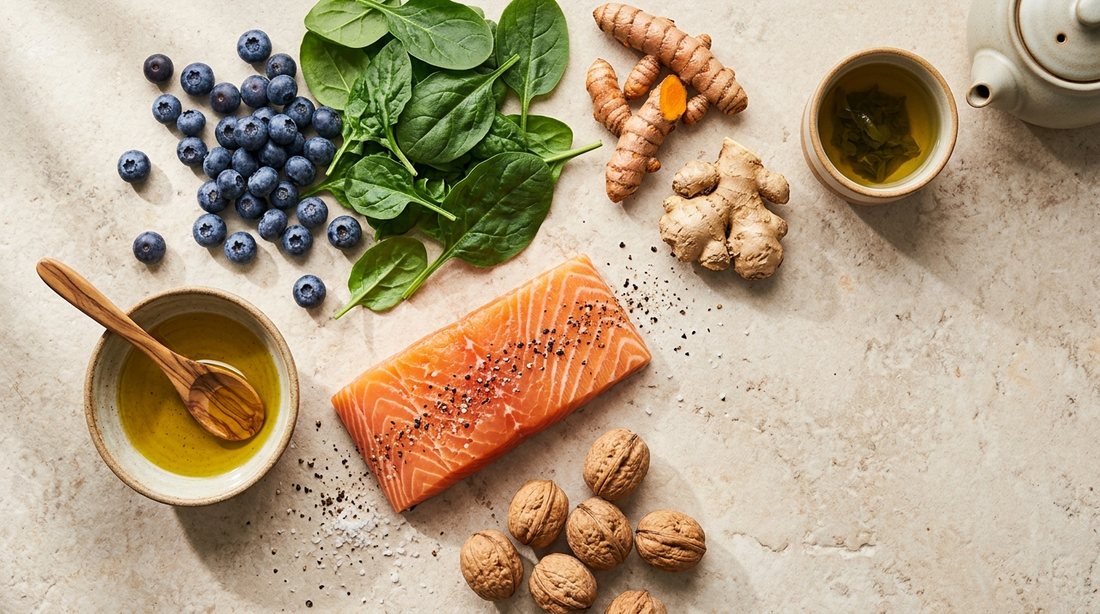 Entzündungshemmende Lebensmittel wie Kurkuma, Ingwer, Beeren, Lachs und Olivenöl auf hellem Untergrund